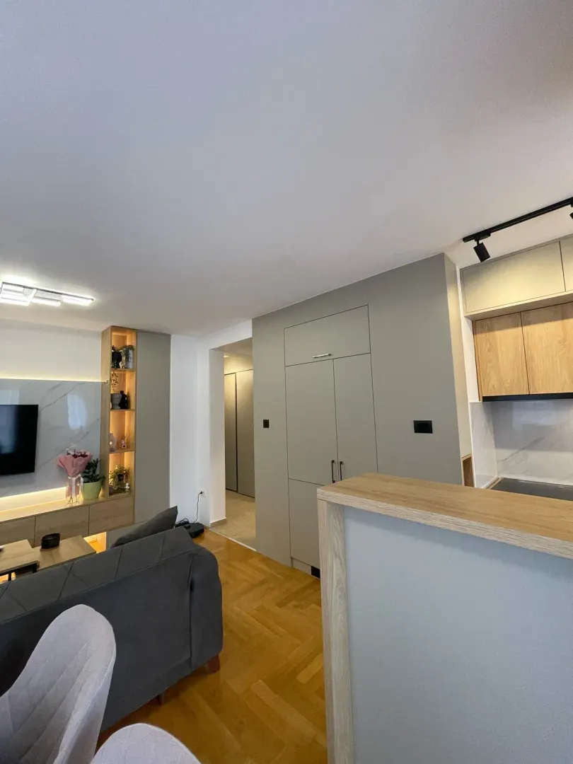 View of the living room with a sofa, TV, and part of the kitchen.