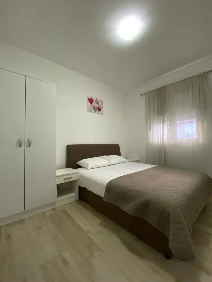 Uređena spavaća soba sa bračnim krevetom, garderoberom i prozorom.