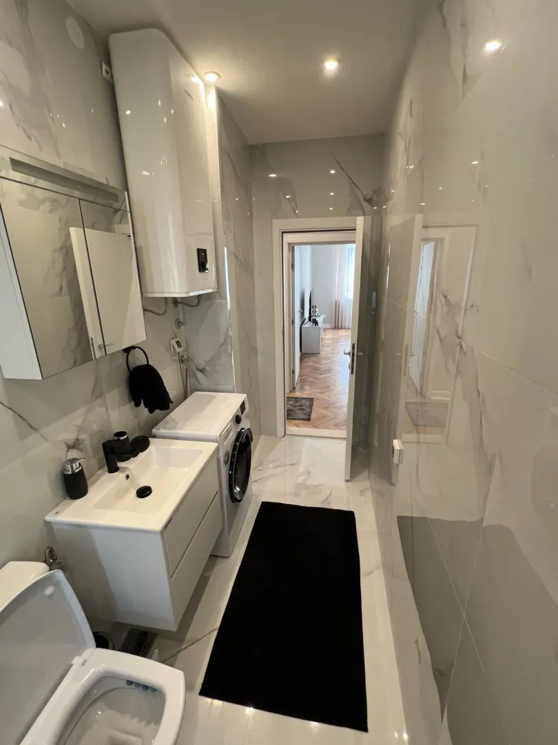 Modern bathroom with light marble tiles, a sink vanity, and a washing machine.