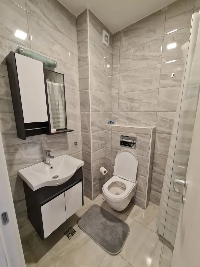 Modern bathroom with grey wall tiles, a toilet, and a sink vanity.