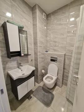 Modern bathroom with grey wall tiles, a toilet, and a sink vanity. - image 9