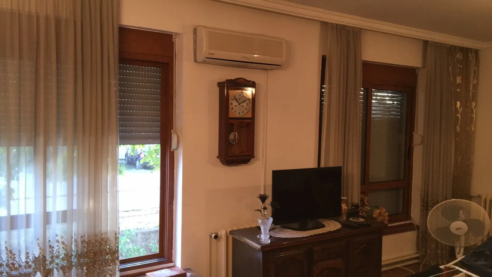 Part of a living room with a cabinet, television, air conditioner, and windows.