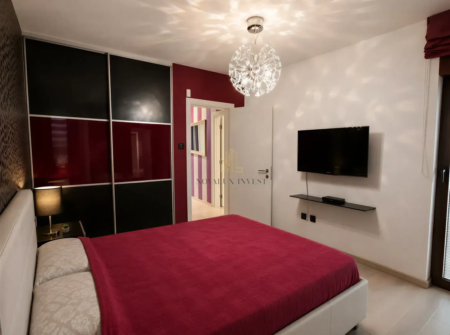 Furnished bedroom with a double bed, large wardrobe, and wall-mounted TV.
