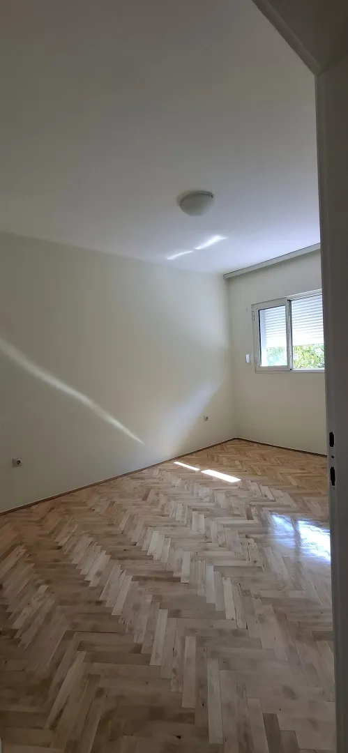Prazna soba sa parketom i prozorom.
