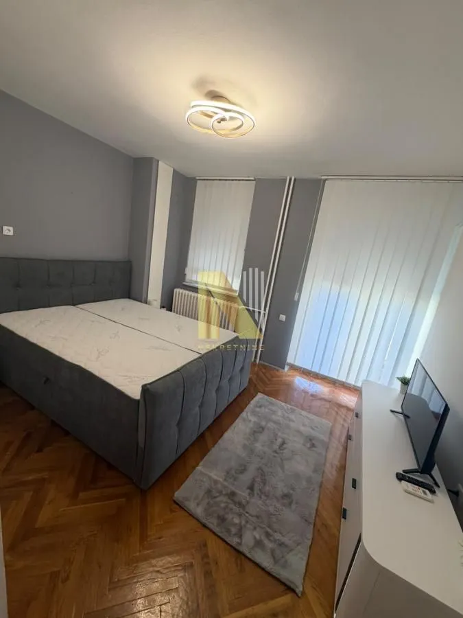 Spavaća soba sa bračnim krevetom, komodom i televizorom.