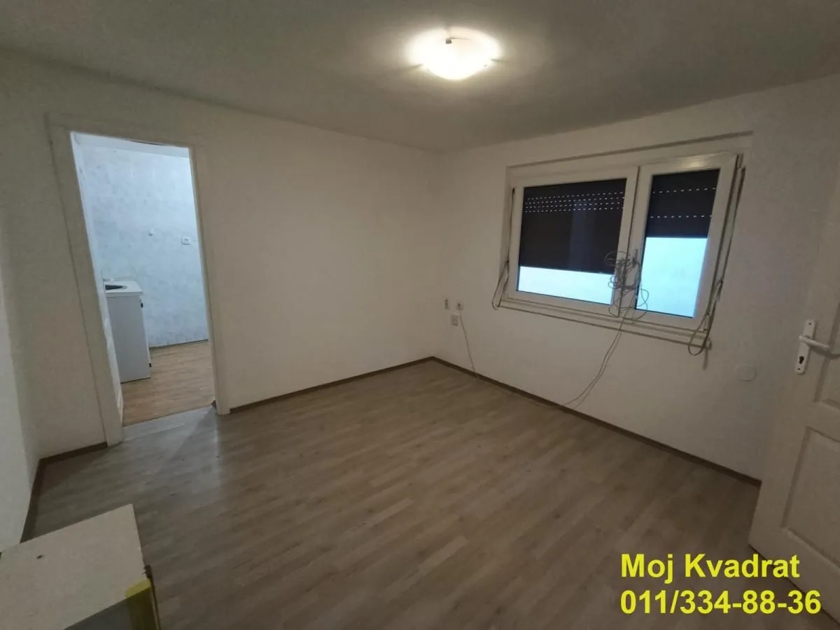 Empty room with laminate flooring and a window, with a view into the adjacent room.