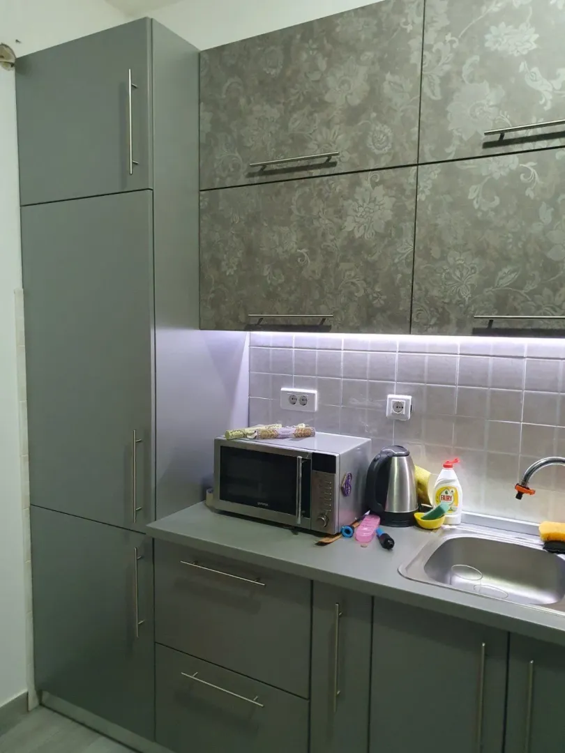 Moderna siva kuhinja sa ugrađenim elementima, mikrotalasnom pećnicom i sudoperom.