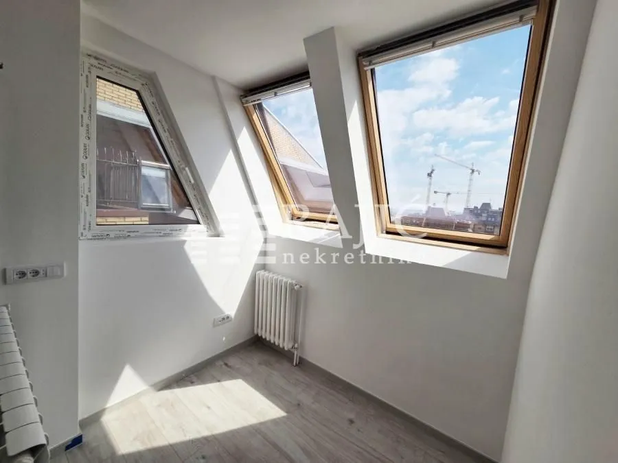 Empty attic room with slanted windows and laminate flooring.