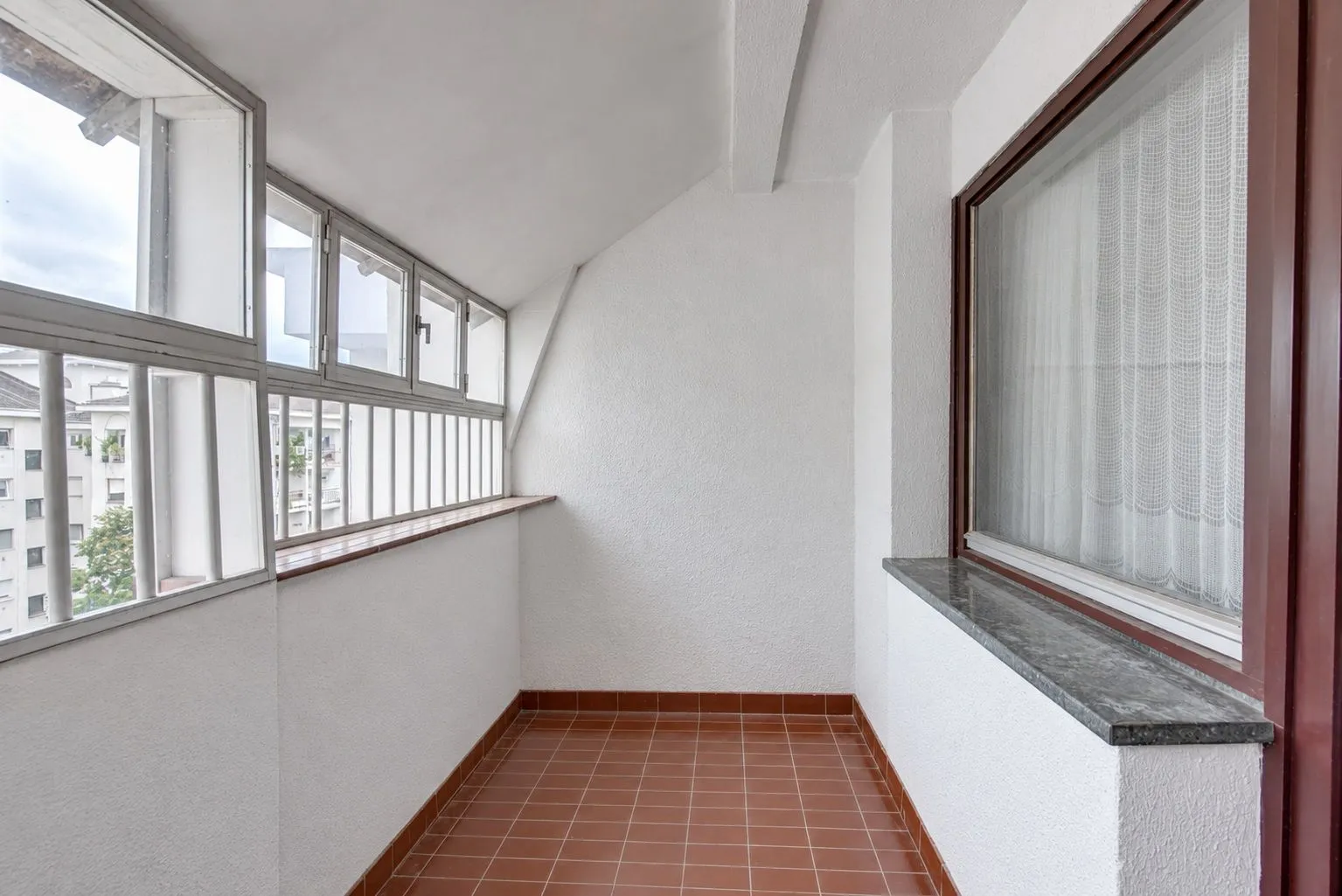Natkriveni balkon sa popločanim podom i velikim prozorima.