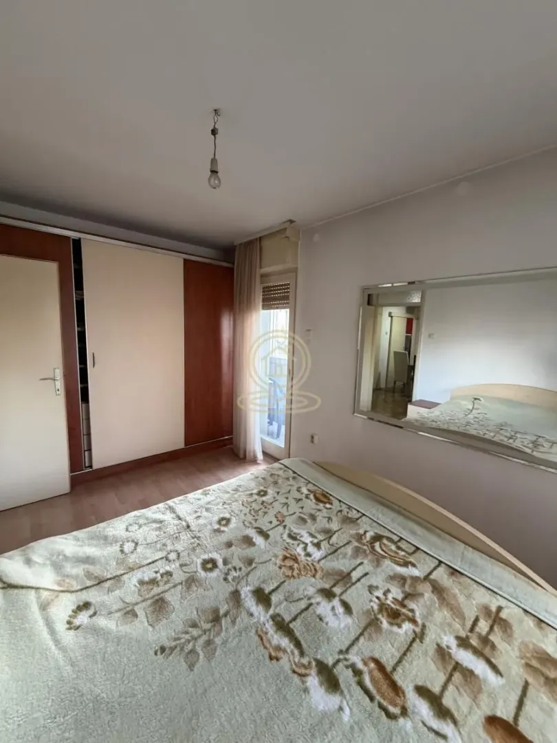 Nameštena spavaća soba sa bračnim krevetom, velikim plakarom i ogledalom na zidu.