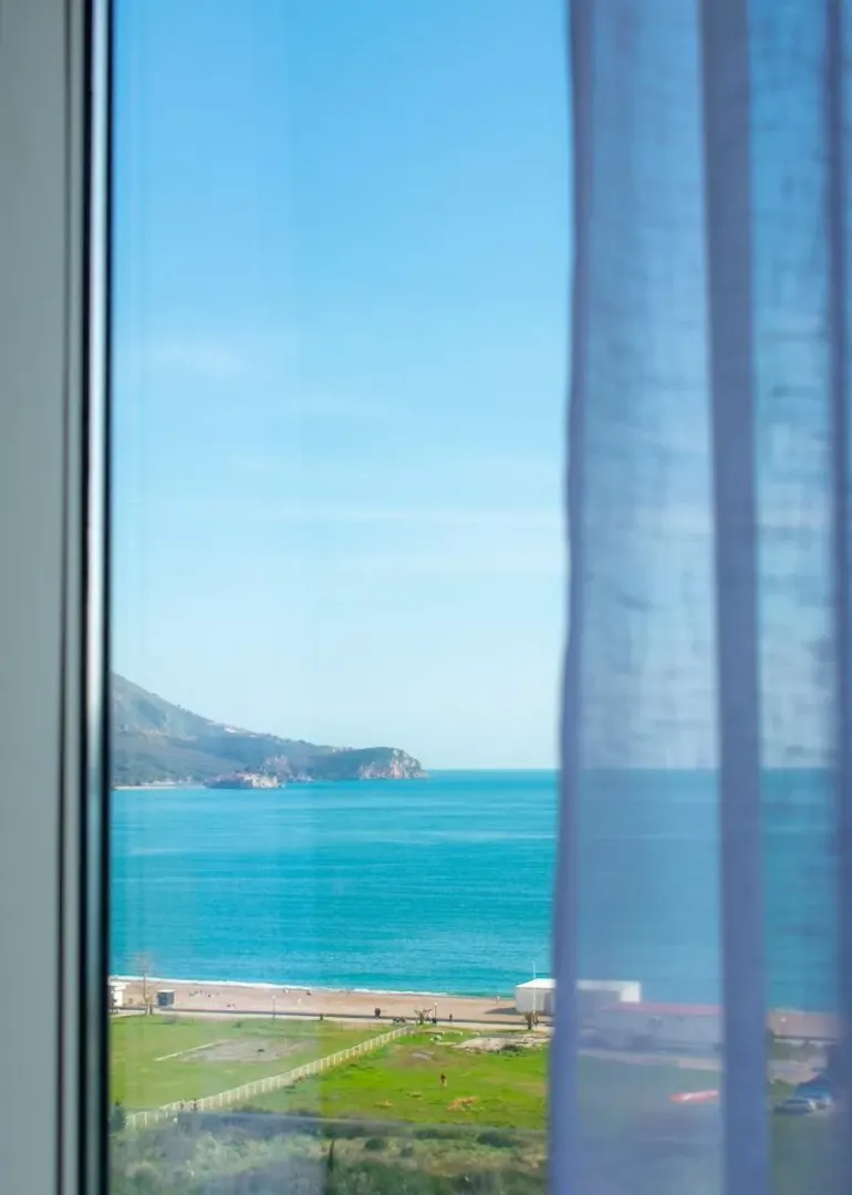 Pogled na more i obalu kroz prozor sa zavesom.