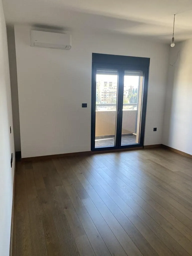 Empty room with wooden flooring, white walls, and access to a balcony.