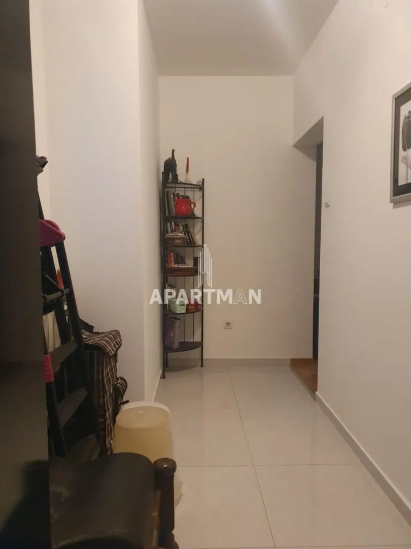 Hodnik sa policom za knjige i svetlim pločicama na podu.