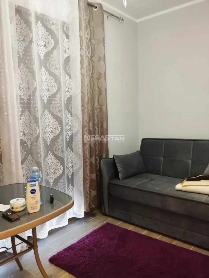 Manja dnevna soba sa tamnosivom sofom i stočićem pored prozora sa zavesama.
