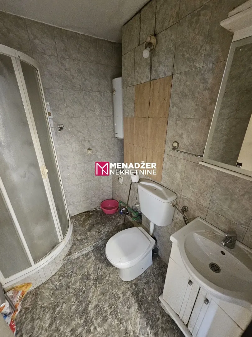 Manje opremljeno kupatilo sa tuš kabinom, lavaboom i WC šoljom.