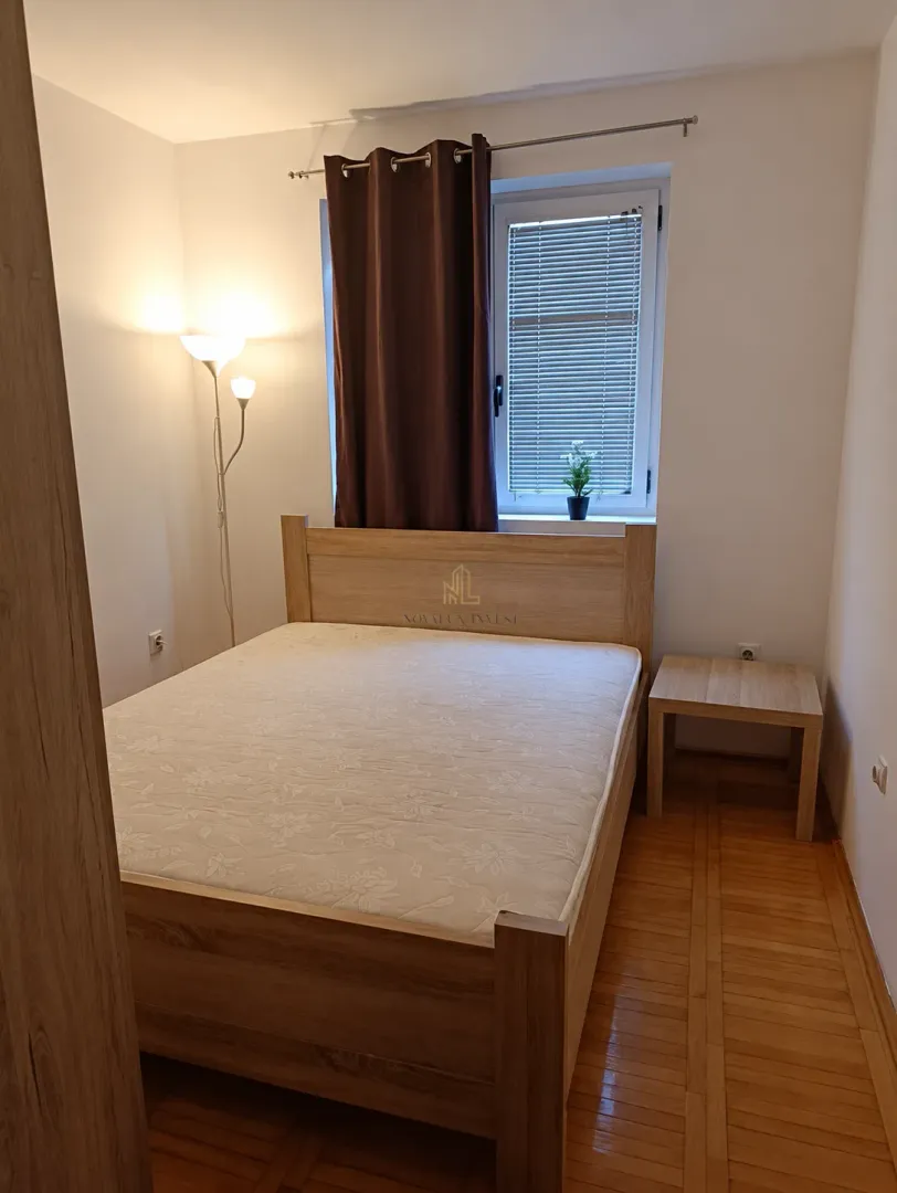 Namještena spavaća soba sa bračnim krevetom, noćnim stočićem i prozorom.