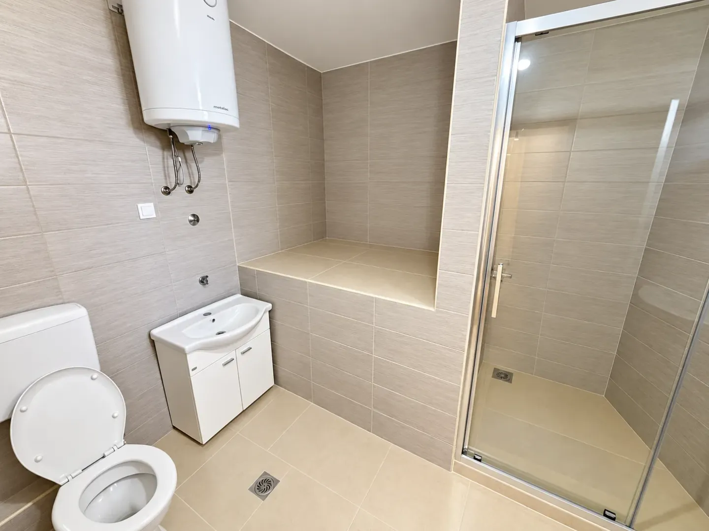 Moderne kupatilo sa tuš kabinom, umivaonikom, WC šoljom i bojlerom.