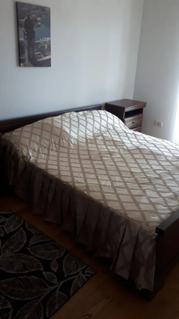 Spavaća soba sa bračnim krevetom, noćnim stočićem i slikom na zidu.