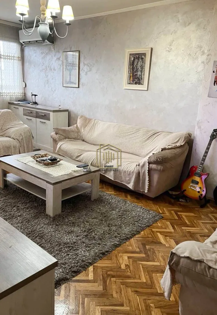 Dnevna soba sa garniturom, stočićem i parketom na podu.