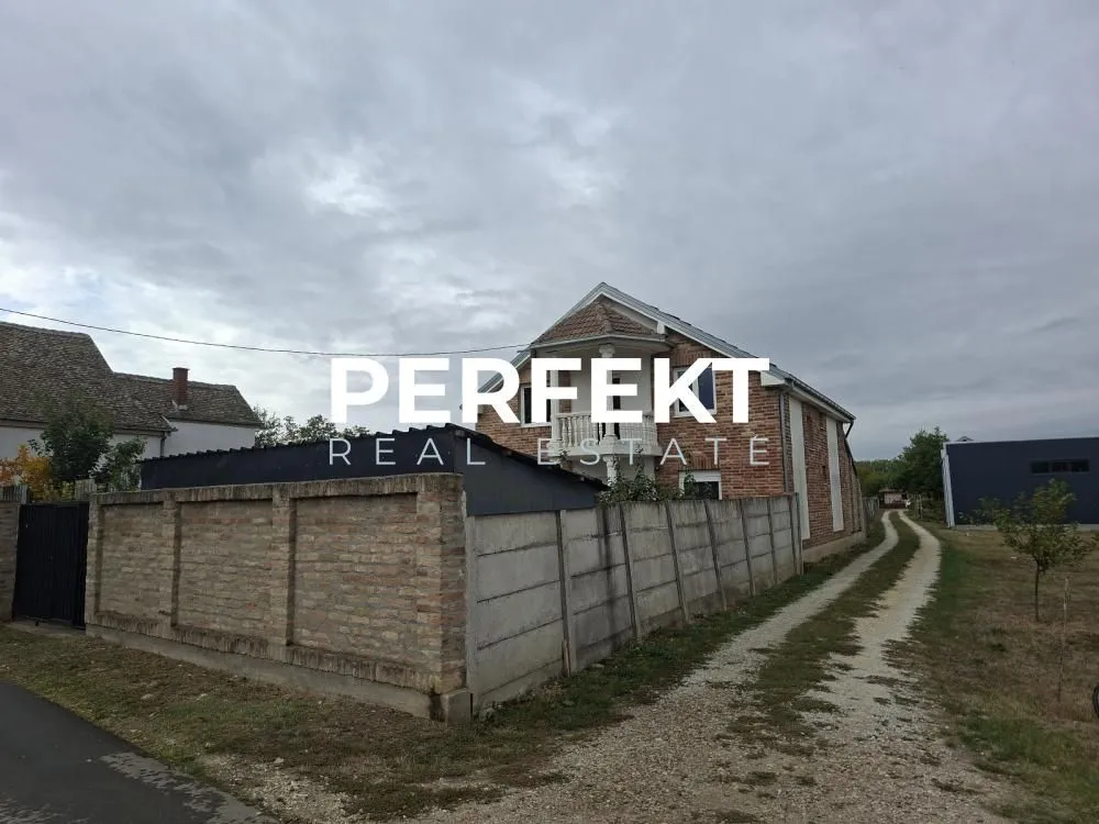 Pogled na spoljašnjost kuće sa dvorištem i ogradom.