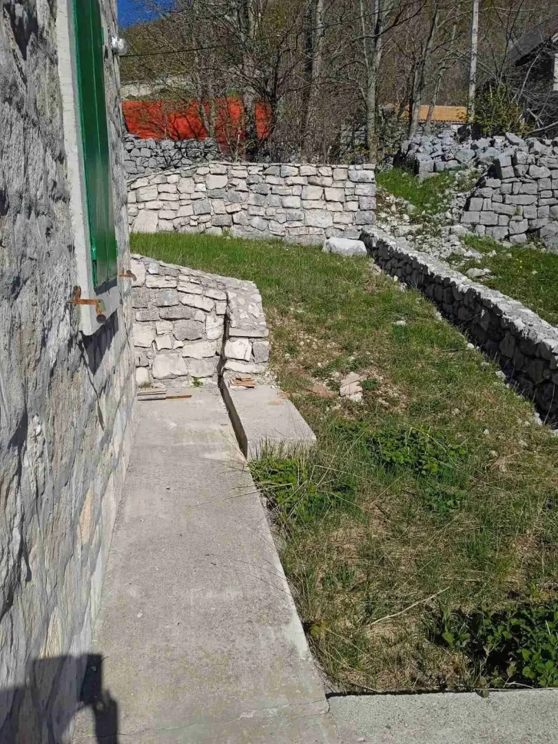Betonska staza i travnato dvorište sa kamenim zidovima pored tradicionalne kamene kuće.