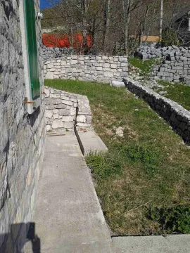 Betonska staza i travnato dvorište sa kamenim zidovima pored tradicionalne kamene kuće. - image 3