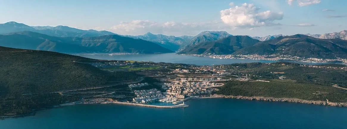 Pogled iz vazduha na primorsko naselje sa marinom i planinama u pozadini.