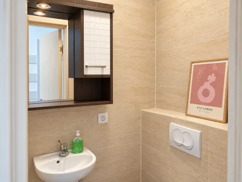 Small bathroom clad in beige tiles with a washbasin, mirror, and concealed cistern. - image 18