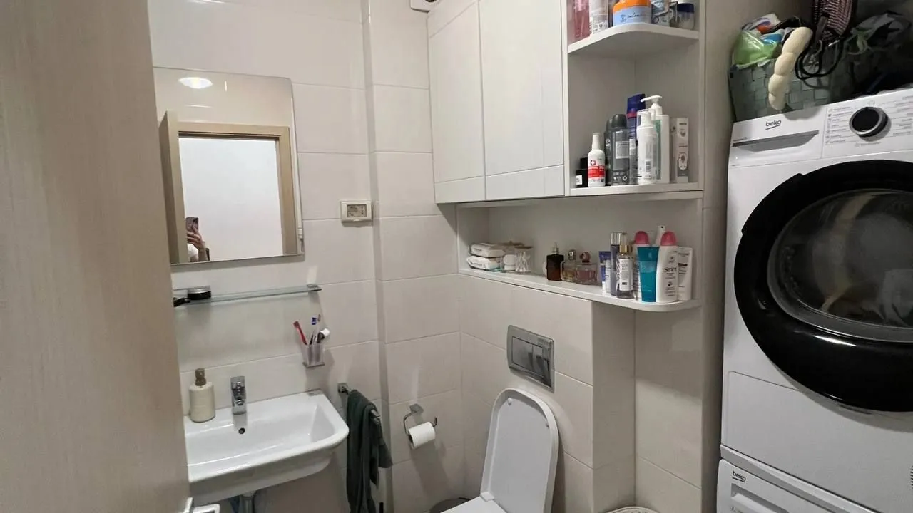 Manje kupatilo sa umivaonikom, WC šoljom, elementima i veš mašinom.