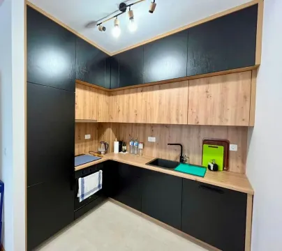 Modern corner kitchen with black units and wooden accents. - image 5