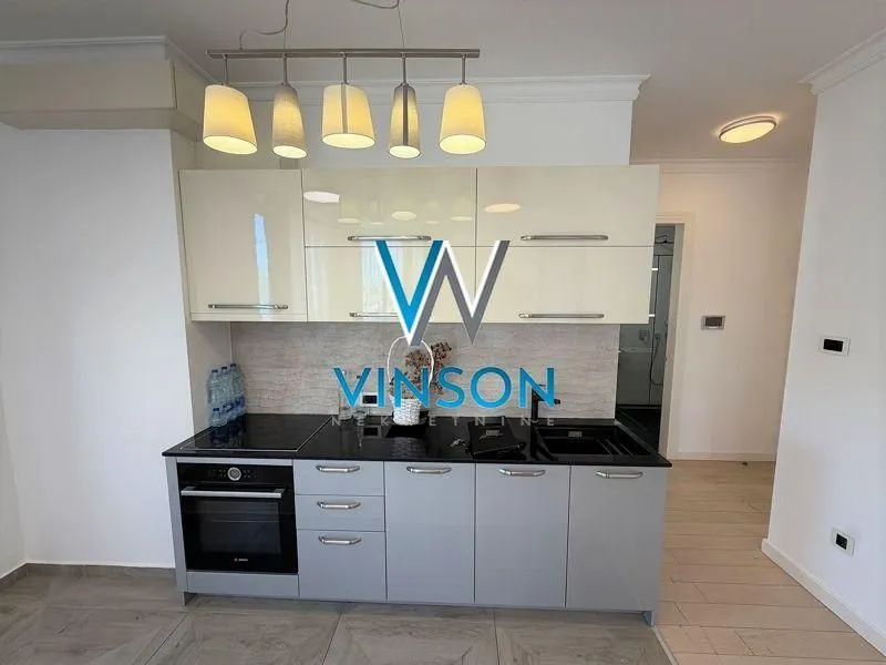 Compact modern kitchen with cream and grey cabinetry and built-in appliances.