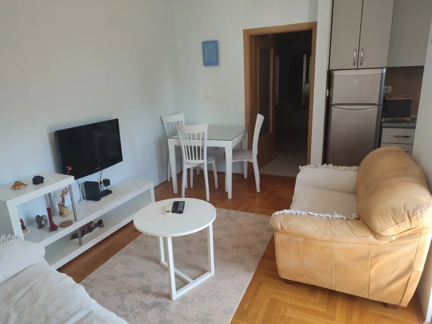 Svijetla dnevna soba sa kožnom garniturom, trpezarijskim stolom i kuhinjskim elementima.