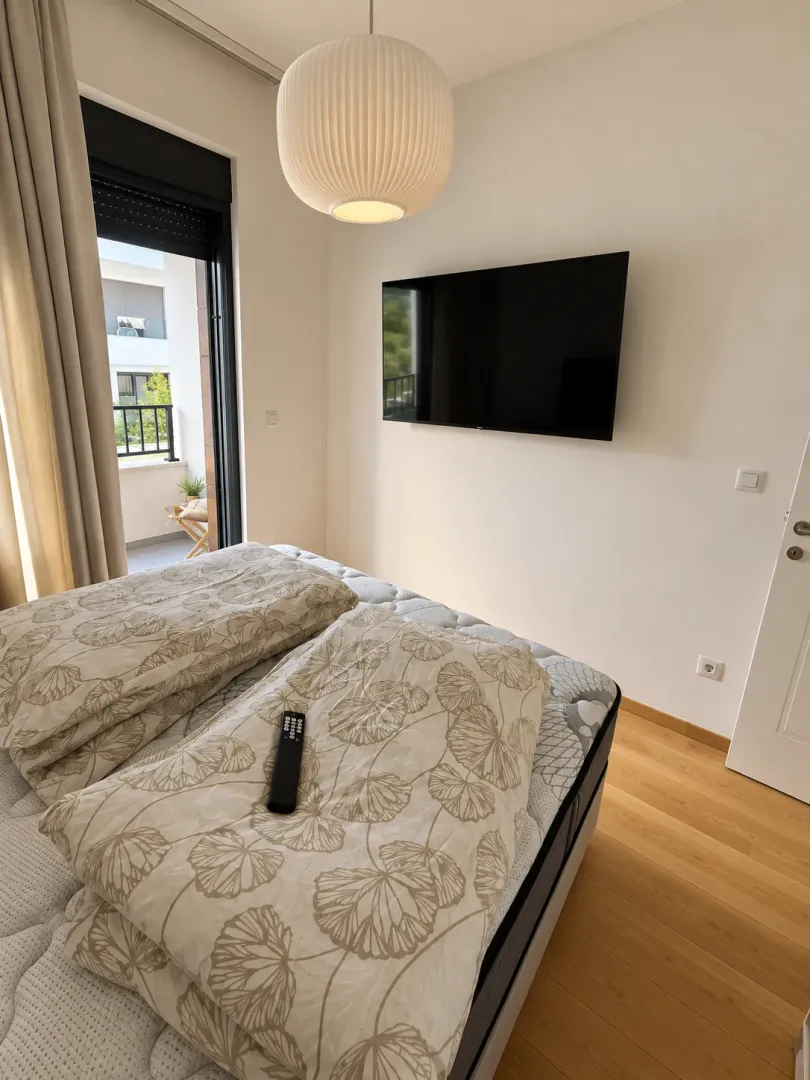 Spavaća soba sa krevetom, zidnim televizorom i izlazom na terasu.