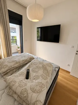 Spavaća soba sa krevetom, zidnim televizorom i izlazom na terasu. - image 9