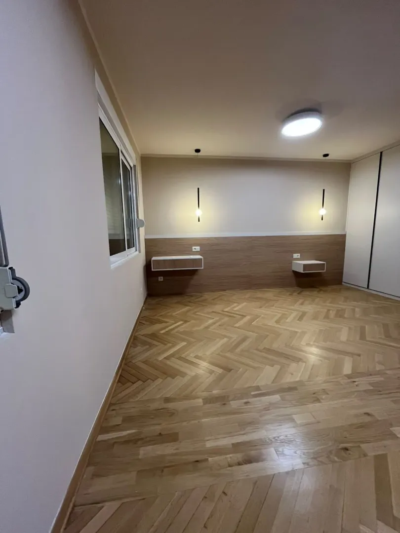 Prazna spavaća soba sa drvenim podom, ugradnim plakarom i zidnim lampama.