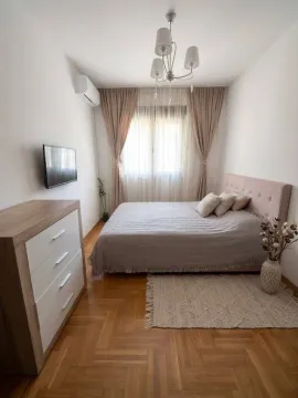 Uređena spavaća soba sa bračnim krevetom, komodom i televizorom na zidu. - image 6