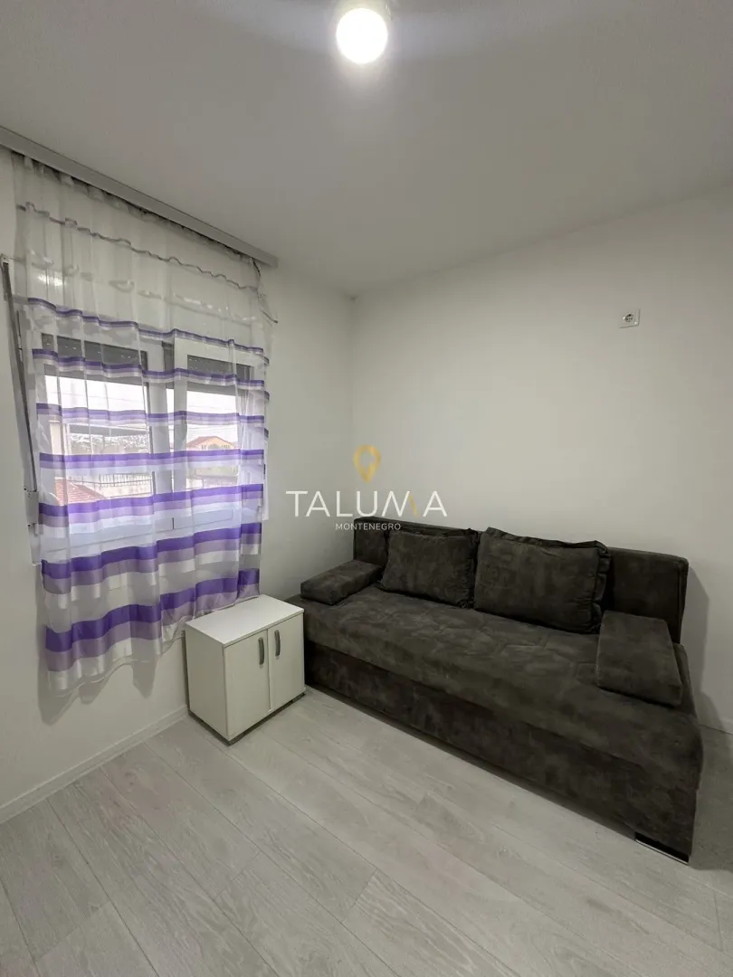 Small living room with a dark sofa, a white cabinet, and a window with curtains.