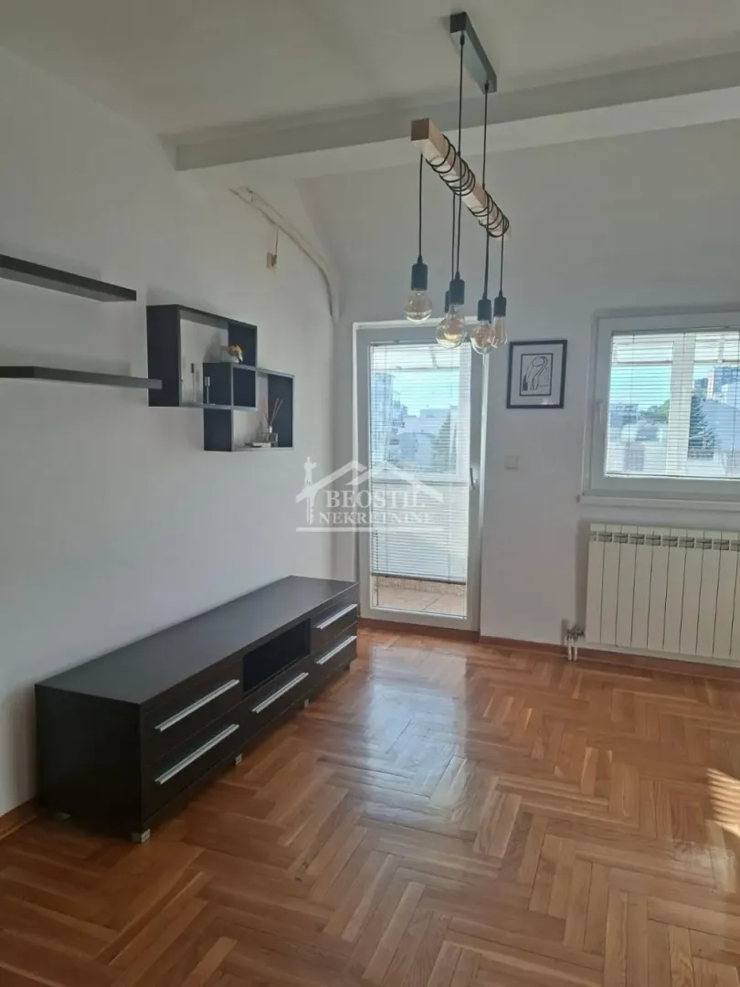 Dnevna soba sa drvenim parketom, TV komodom i izlazom na terasu.