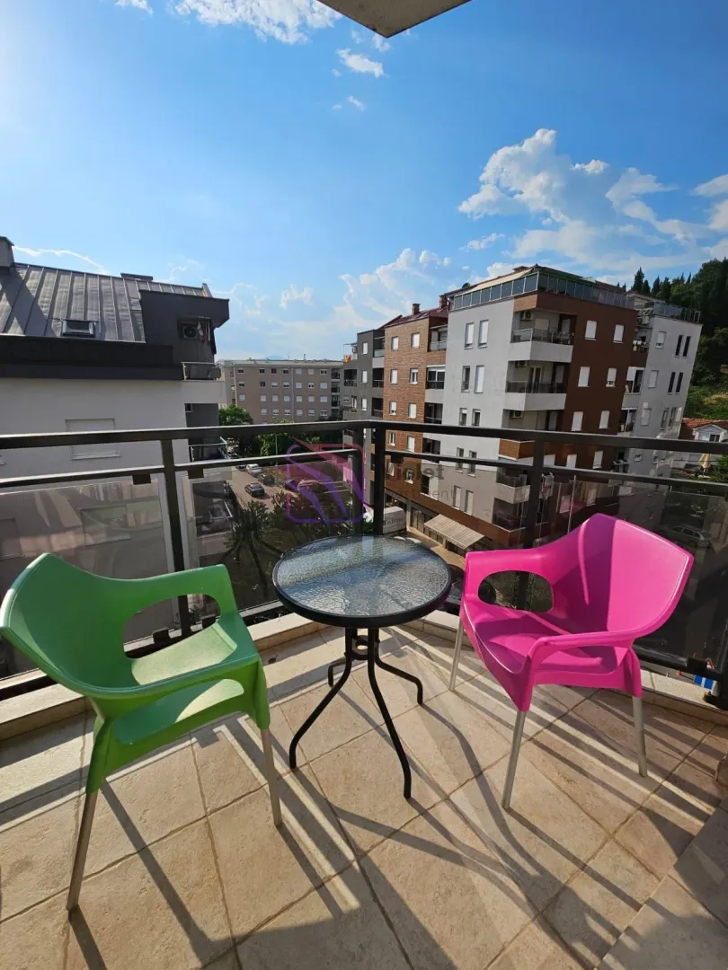 Manji namješteni balkon sa stolom i dvije stolice i pogledom na grad.