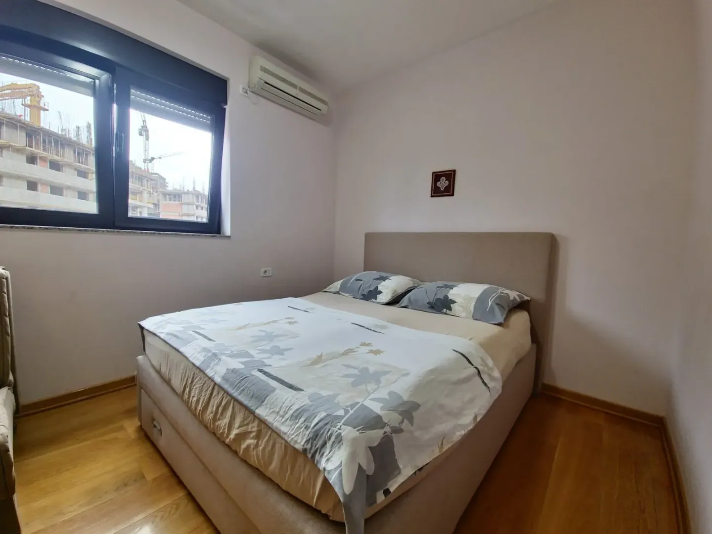 Spavaća soba sa bračnim krevetom, drvenim podom i prozorom.