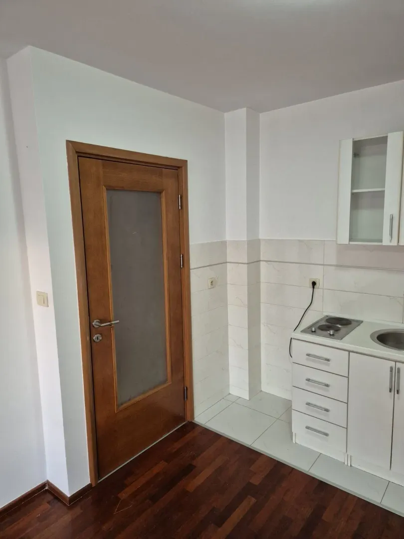 A small kitchen with white cabinets next to a wooden door.