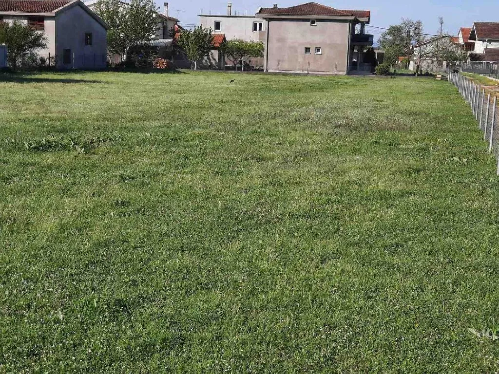 Ravan travnati plac u naselju sa okolnim kućama.