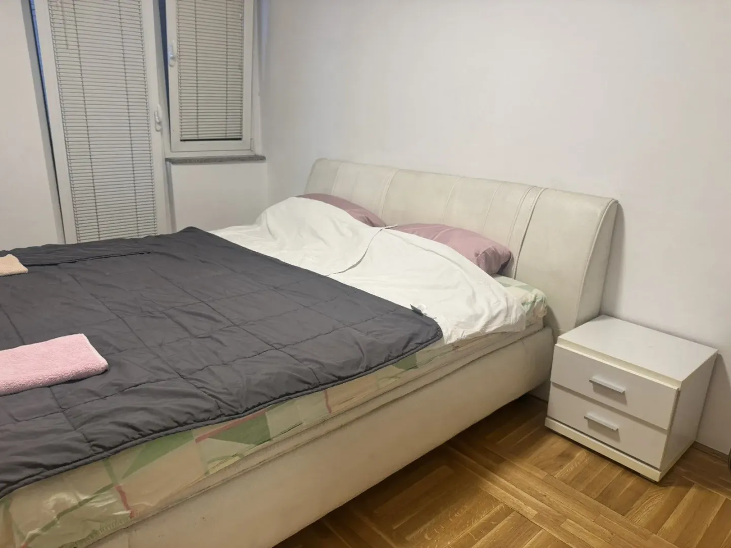 Spavaća soba sa bijelim bračnim krevetom i noćnim ormarićem.