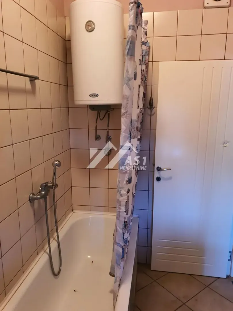 Manje kupatilo sa kadom, bojlerom i zavesom za tuširanje.
