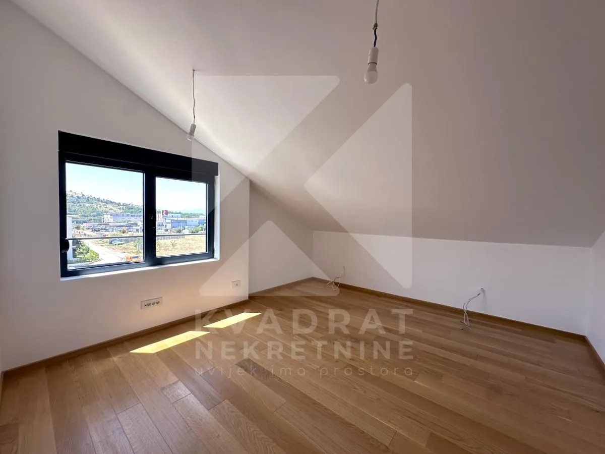 Empty attic room with hardwood floors and a window.