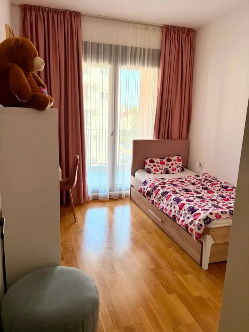 Dječija soba sa krevetom, radnim stolom i balkonskim vratima.