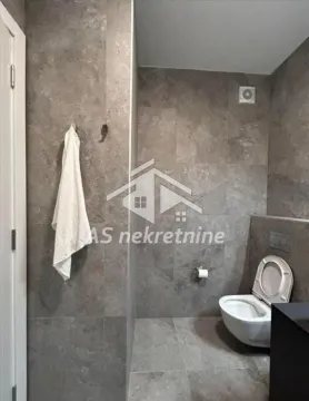 Small bathroom lined with grey tiles featuring a toilet and a towel rack. - image 17
