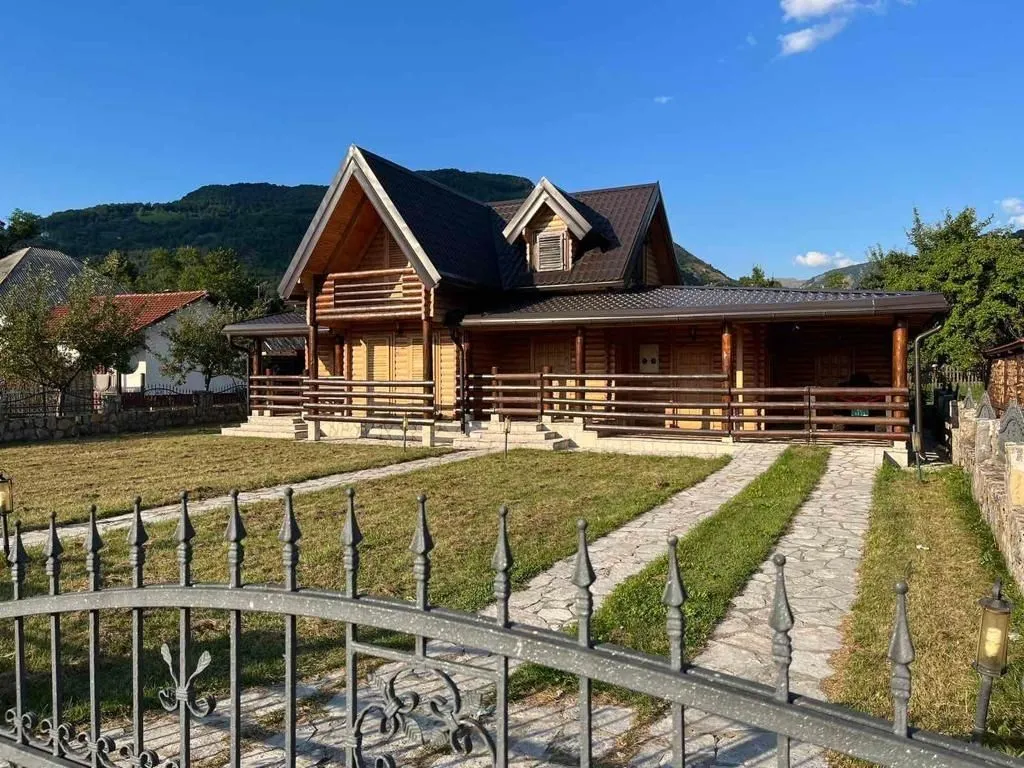 Drvena kuća sa uređenim dvorištem i popločanom stazom.
