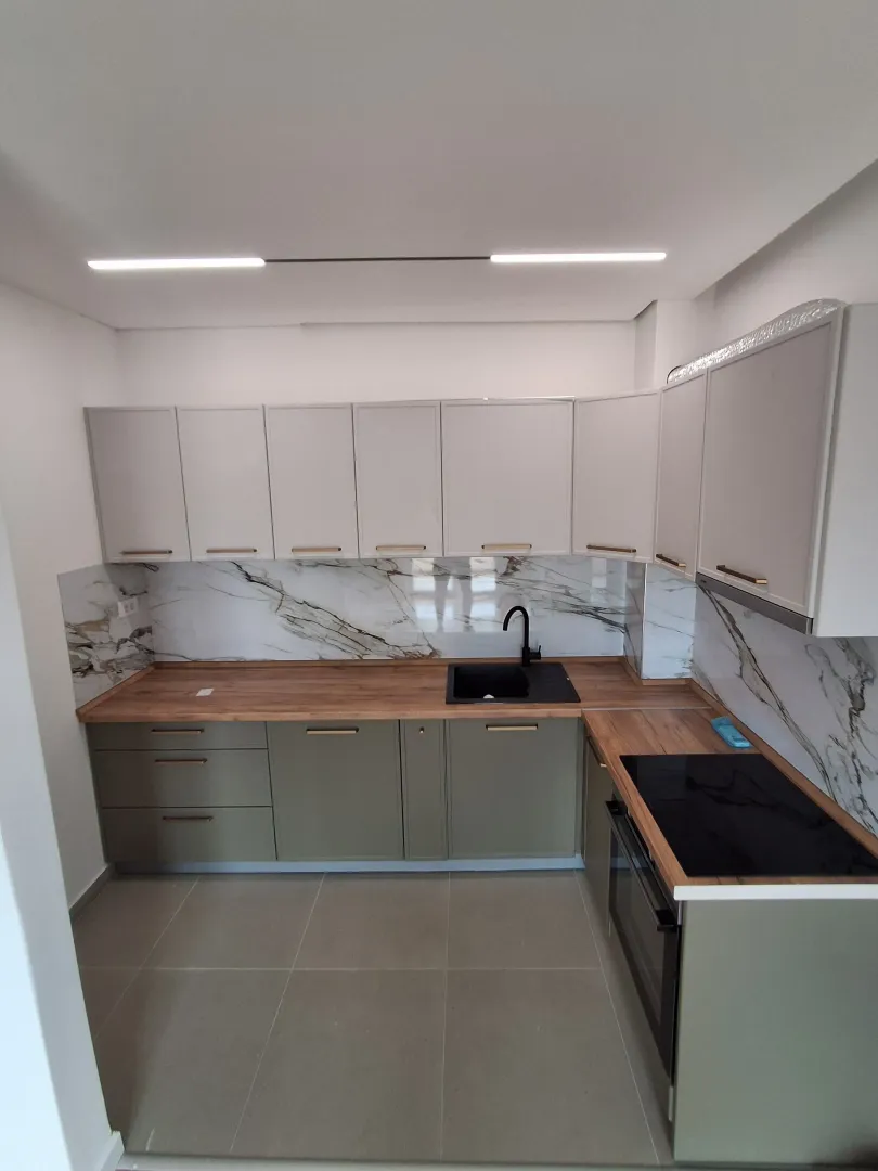 Modern kitchen with light cabinets, wooden countertop and marble-patterned backsplash.