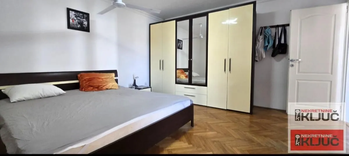 Furnished bedroom with a double bed, large wardrobe, and wooden parquet flooring.
